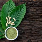 Mitragyna speciosa or kratom leaves with medicinal products in capsules and powder in white ceramic bowl and wooden table, top view